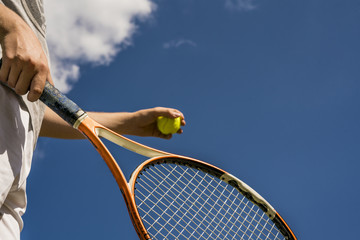 tennis player man hand making a shot holding a ball and a racket against sky