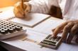 © kanchitdon - Businessman using calculator and writing note and calculate finance in the room.