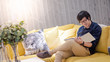 © zephyr_p - Young Asian man reading book on sofa in living room. Lifestyle in living space concept
