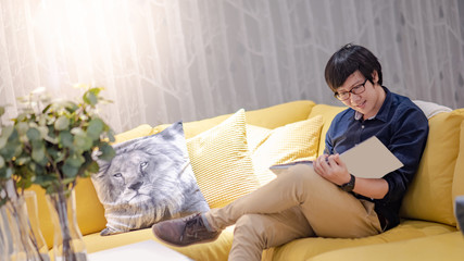 Young Asian man reading book on sofa in living room. Lifestyle in living space concept