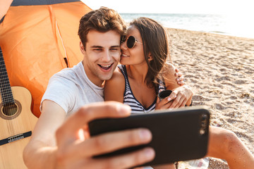 Wall Mural - Cute loving couple make selfie by mobile phone on the beach outdoors.