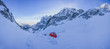 A red tent pitched up on snow in the middle of winter alpine landscape. Winter camping on snow. High alpine peaks, blue sky and bivi tent in winter alpine environment. Adventure and extreme alpinism.