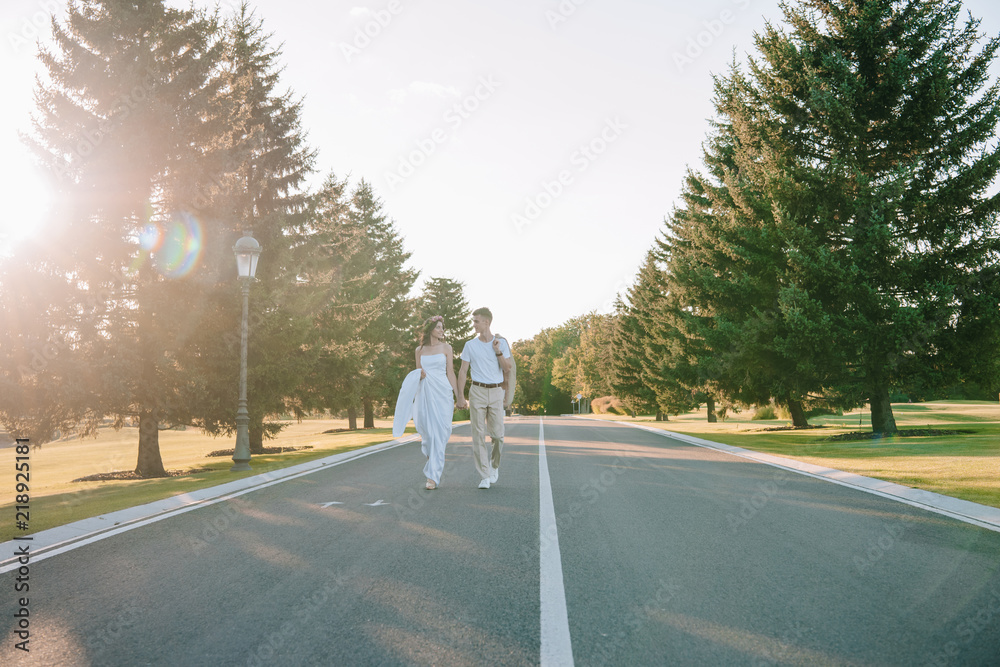 young wedding couple holding hands and smiling each other while walking ...