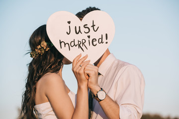 young wedding couple kissing and holding heart with just married inscription