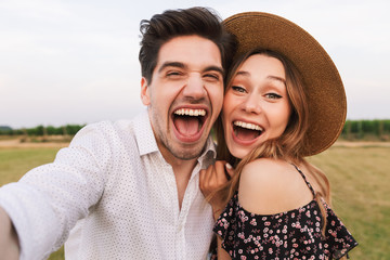 Canvas Print - Photo of excited young man and woman dating, and taking selfie together while walking outdoor in countryside