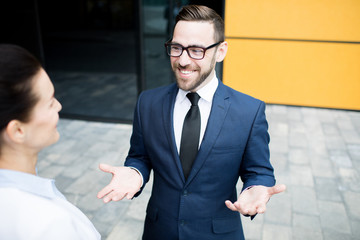 Man in blue suit standing with palms up talking with woman smiling