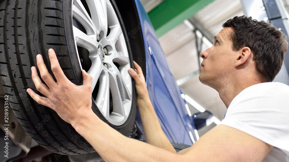 Reifenwechsel in einer autowerkstatt // tyre change in a car repair shop - worker assembles rims on the vehicle - obrazy, fototapety, plakaty 