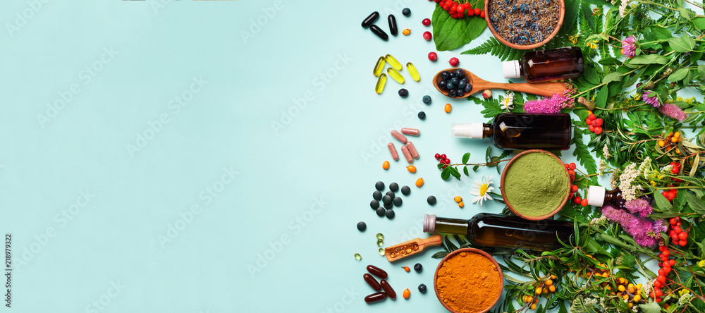 Holistic medicine approach. Healthy food eating, dietary supplements, healing herbs and flowers. Turmeric, dried lavender, spirulina powder in wooden bowls, fresh berries, omega acid capsules - obrazy, fototapety, plakaty 