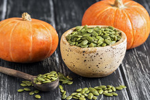 Bowl With Raw Pumpkin Seeds On A Rustic Black Table. Small Orange Pumpkins. Selective Focus