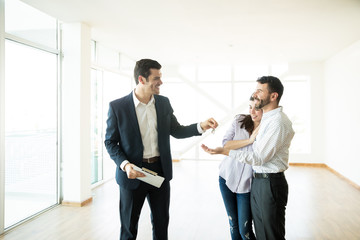 Smiling Realtor Giving Keys To Couple After Successful Housing Purchase