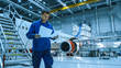 © Gorodenkoff - Aircraft maintenance mechanic in blue uniform is going down the stairs while reading papers in a hangar.