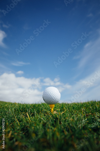 Fototapety Golf  pilka-golfowa-na-tee-zielonej-trawie-i-niebieskim-tle-nieba