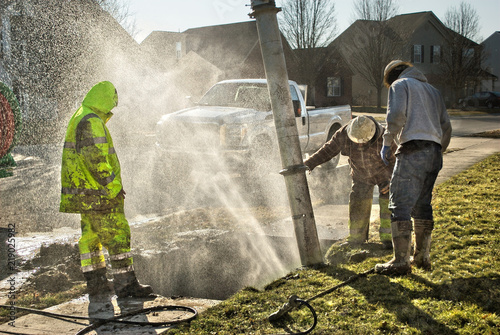 Fotografía Muddy utility worker men fixing broken water line with droplets spraying into the air