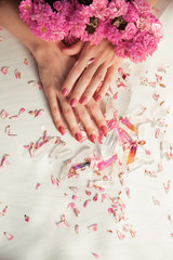 Beautiful woman hands with perfect violet nail polish on white wooden background holding little quartz crystals, decorated with rose leaves, healing crystal concept shoot, can be used as background 