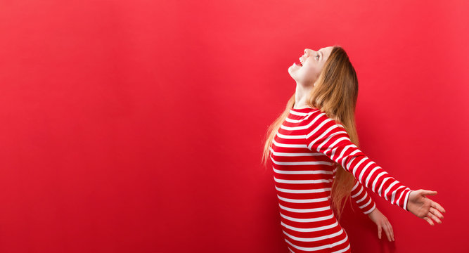 Happy young woman with her arms outstretched on a red background
