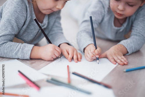 Fototapeta Children lie on the floor in pajamas and draw with pencils. Cute child painting by pencils.Hand of child girl and boy draw and paint with crayon. Close up view