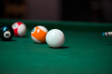 Wall Mural - Sport billiard balls on green billiard table in pub. Player is about to hit the ball, focusing on his shot. On going billiard game. Competitive players trying to find out the winner of the round.