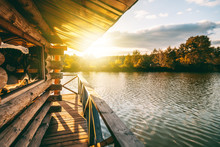 Wooden House With A Terrace On The Water At The Lake, At Sunset, A Beautiful River Bank At Sunset