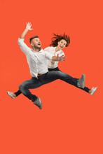 Freedom In Moving. Pretty Young Couple Jumping Against Red Background