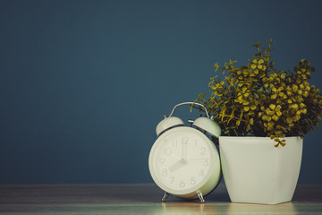 Wall Mural - Little decorative tree and flower bouquet in white vase with vintage alarm clock on wooden table with copy space.