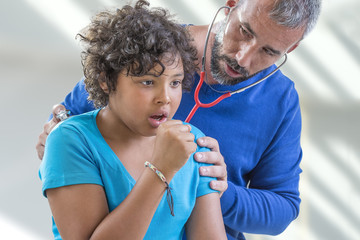 young boy flu. doctor examines a young teen boy colds listen to the lungs with a stethoscope while he is ccoughing