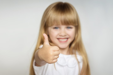 little blonde girl in white dress smiles and shows thumb up. focus on the finger