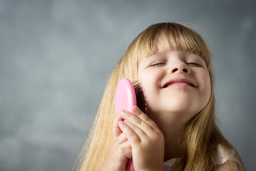 Wall Mural - little blonde girl with long hair combs her hair with a pink comb