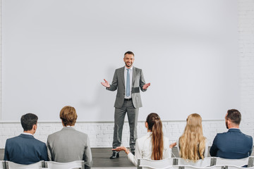 handsome business coach standing on stage and gesturing during training in hub