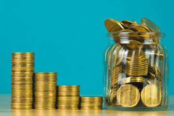 Coins stacks and gold coin money in the glass jar on table with green background, for saving for the future banking finance concept.