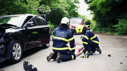 Wall Mural - Firefighters rescuing a young injured woman lying on the road after an accident.