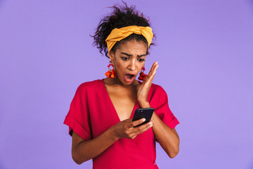 Poster - Shocked african woman in dress using smartphone with open mouth