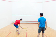 Rear View Of Two Competitive Young Men With A Modern Lifestyle Playing Doubles Squash Game On A Professional Court
