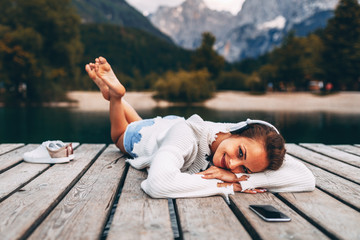 Sticker - Attractive young woman listening to music via wifi headphones and smartphone on the lake