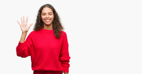 Young hispanic woman wearing red sweater showing and pointing up with fingers number five while smiling confident and happy.