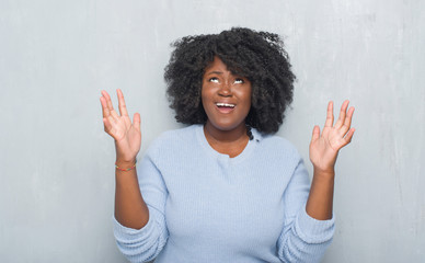 Canvas Print - Young african american woman over grey grunge wall wearing winter sweater crazy and mad shouting and yelling with aggressive expression and arms raised. Frustration concept.