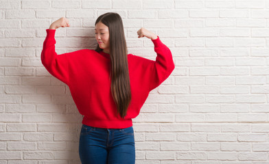 Sticker - Young Chinese woman over brick wall showing arms muscles smiling proud. Fitness concept.