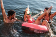 © BalanceFormCreative - Young friends swimming and having fun in the lake.Female sitting on air mattress drinks lemonade  and having fun with friends.