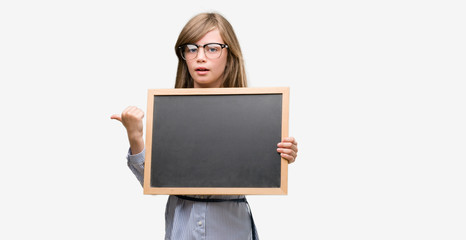 Sticker - Young blonde child holding blackboard pointing with hand and finger up with happy face smiling