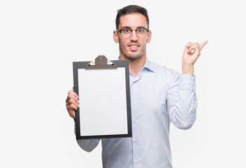 Sticker - Handsome young business man showing a clipboard very happy pointing with hand and finger to the side