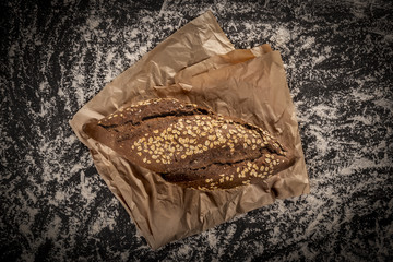 Wall Mural - From above shot of big rye loaf with oats on piece of parchment paper on top of table in white flour