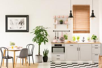 real photo of bright kitchen interior with checkerboard floor, pastel pink accessories, fresh plants
