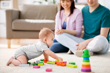 Wall Mural - family, parenthood and people concept - happy mother, father and baby boy playing toy blocks at home
