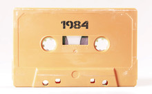 A Vintage Cassette Tape From The 1980s Era (obsolete Music Technology) Labeled 1984 (my Addition, Not In The Original Image). Color: Cream, Sand. White Background.
