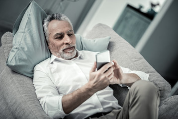 Wall Mural - Receiving message. Concentrated retired man lying on his couch while checking email