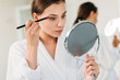 © LIGHTFIELD STUDIOS - beautiful young woman holding mirror and applying eyeshadow