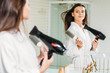© LIGHTFIELD STUDIOS - beautiful young woman holding hair brush and drying hair at mirror in bathroom