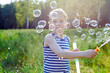 © Sergios - Little blond boy makes bubbles soap outside in a park