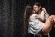 © LIGHTFIELD STUDIOS - portrait of young man holding girlfriend in white shirt while standing under rain isolated on black