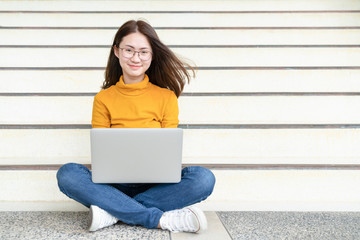 Happy young woman sitting on the floor with crossed legs and using laptop on gray background, Portrait of a happy young woman sitting on the city stairs and using laptop computer outdoors