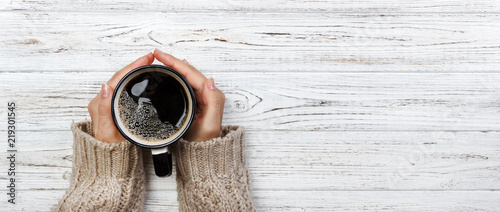 Plakaty do kawiarni woman-holding-cup-of-hot-coffee-on-rustic-wooden-table-closeup-photo-of-hands-in-warm-sweater-with-mug-winter-morning-concept-top-view-banner